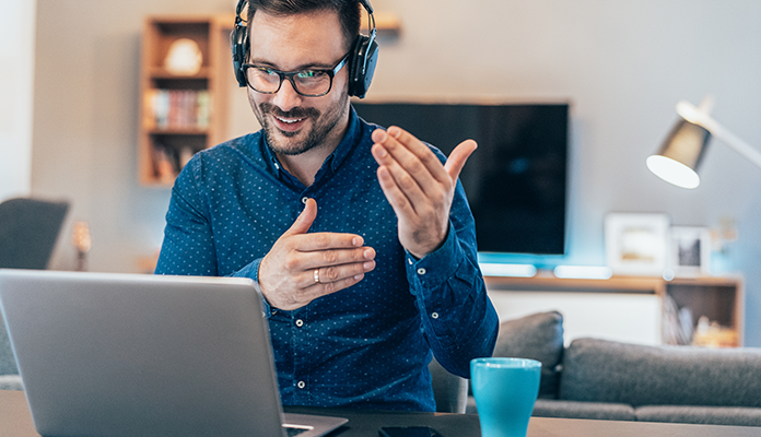 Ein Referent sitzt in eine modernenUmgebung vor seinem Laptop und hält gestenreich einen Online-Vortrag.