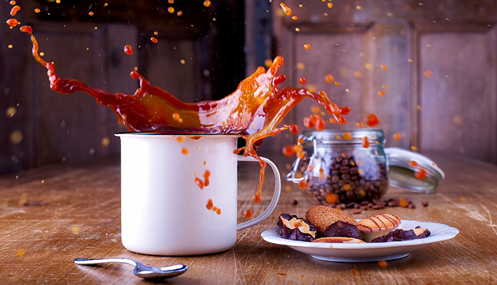 Ein Holz-Tisch auf dem Kekse und eine Tasse Kaffee stehen. Ein Keks ist gerade in die Kaffeetasse gefallen und der Kaffee spritzt weite aus der Tasse.