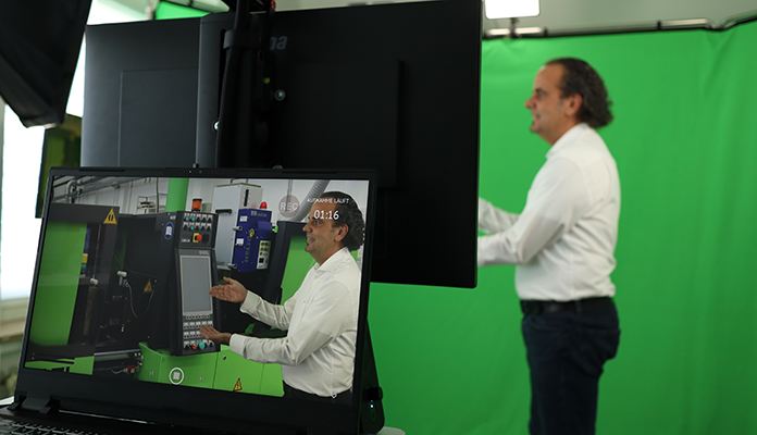 Blick in das Greenscreenstudio. Vor dem Greenscrenn steht der Sprecher und erklärt eine virtuell eingefügte Spritzgussmaschine. Auf einem Laptop sieht man die fertige Szene.